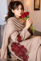 A woman wearing a beige salwar suit with red floral embroidery and holding red roses, posed in an indoor setting.