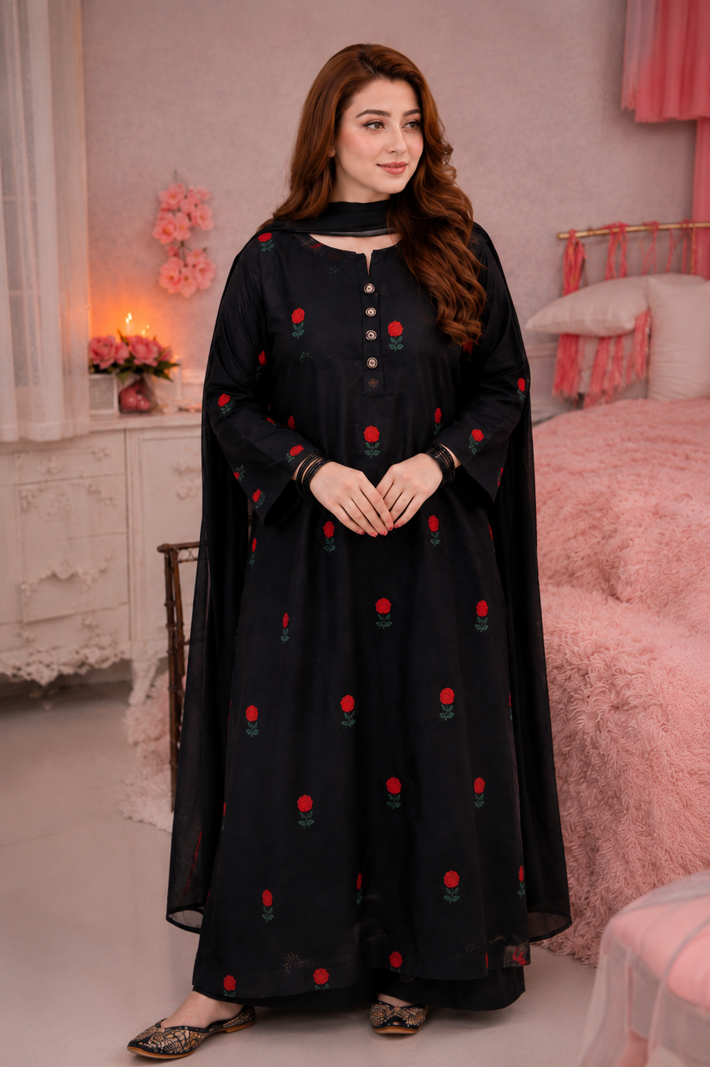 A woman wearing a black long kurta with red rose embroidery and a matching black dupatta, standing in a pink bedroom setting.
