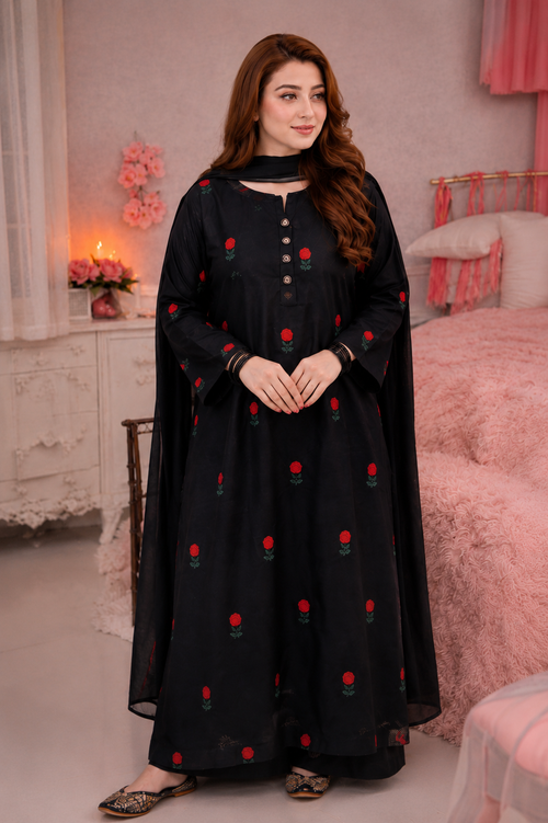 A woman wearing a black long kurta with red rose embroidery and a matching black dupatta, standing in a pink bedroom setting.