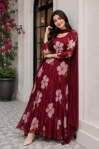 A woman models a long maroon anarkali-style dress with pink floral prints and a matching draped dupatta, standing in a courtyard setting.