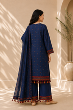 A woman stands with her back to the camera wearing a navy blue traditional outfit with small embroidered motifs and a matching dupatta, set against a warm beige background with soft window shadows.