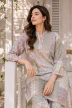 A woman wearing a light pastel printed kurta and matching trousers, leaning on a white railing in a sunlit outdoor setting with soft floral shadows.