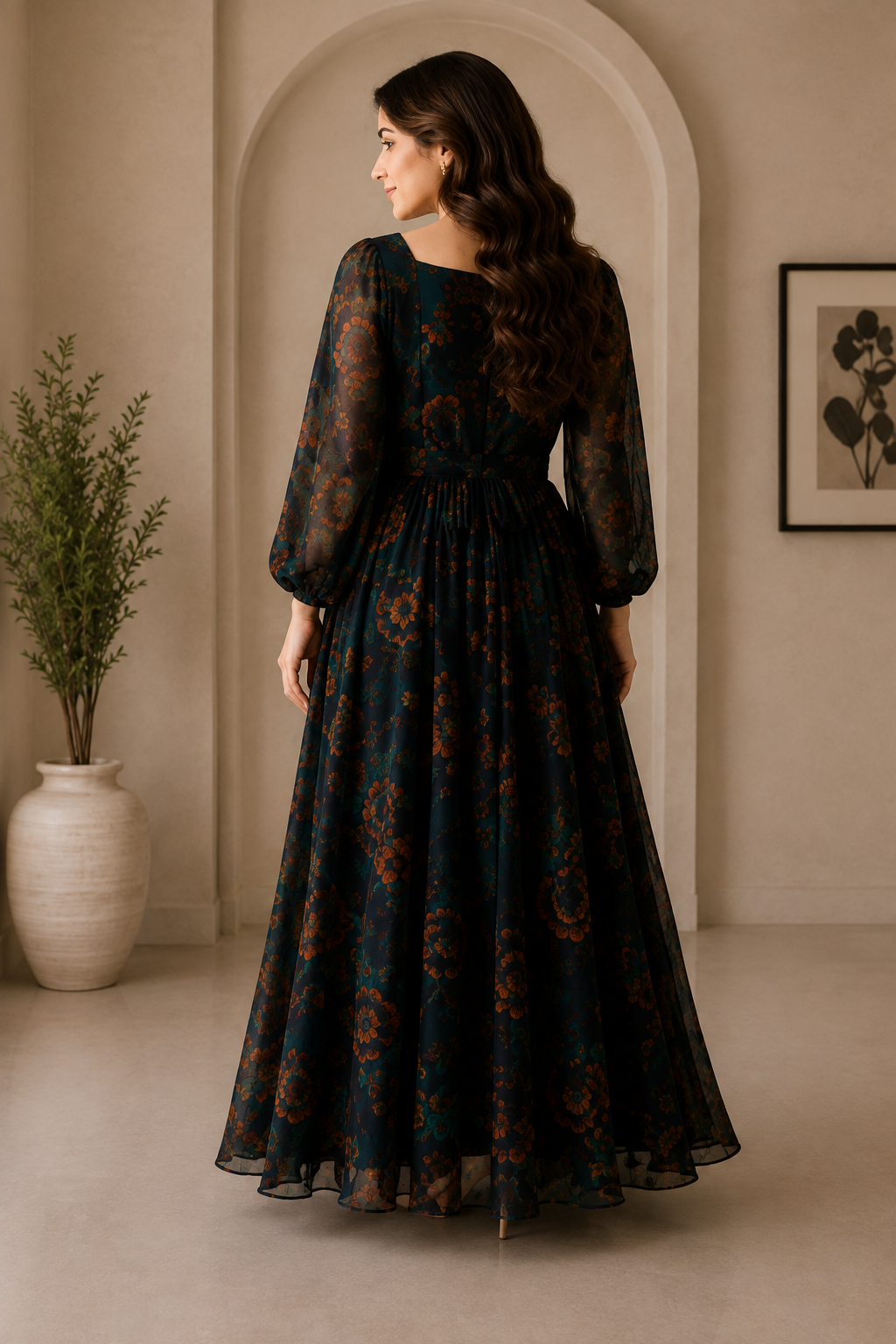 A woman stands in profile wearing a long dark teal maxi dress with a rust-orange floral pattern, photographed in a warm neutral-toned interior with an arched doorway and potted plant.