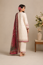 A woman modeling a traditional three-piece salwar kameez suit in cream with pink and red embroidery, paired with a deep pink printed dupatta, standing in profile against a neutral beige background.